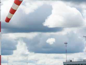 An airport scene with a windsock prominently displayed against a cloudy sky